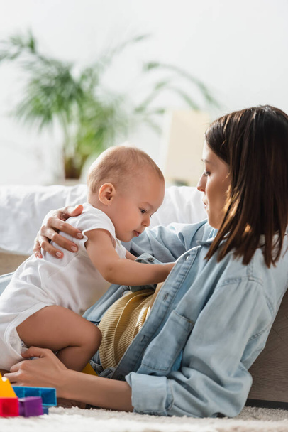 брюнетка женщина играет с малышом сыном на полу дома - Фото, изображение