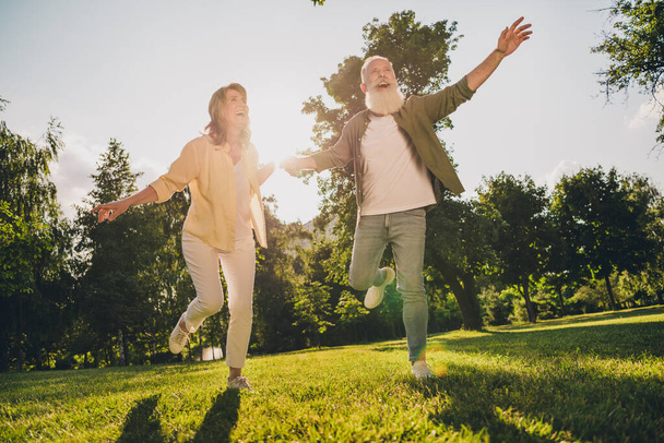 Full length photo of happy joyful old people feel young run green nature summer hands hold enjoy outside outdoors in park - Foto, imagen