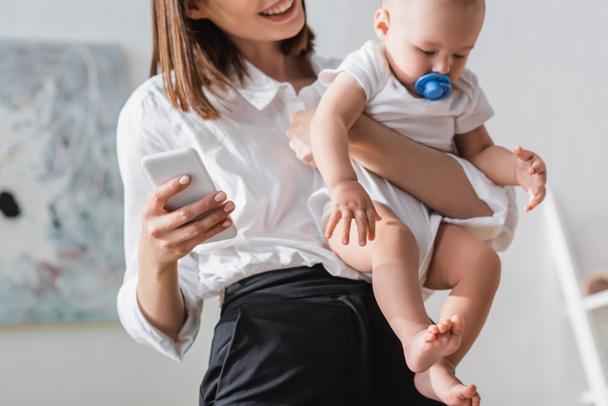 blurred woman holding smartphone and little son in romper - 写真・画像