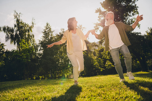 Full length photo of mature couple hold hands romantic forest go run green grass nature spring outdoors - 写真・画像