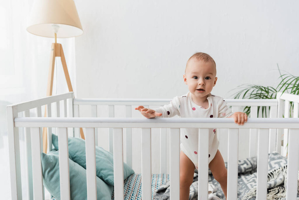 toddler boy looking at camera while standing in crib - Photo, Image