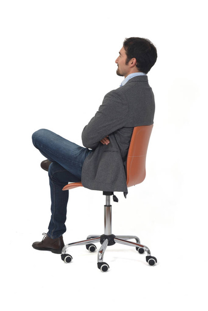 rear view of a man with blazer sitting on chair arms and legs crossed on white  background - Foto, Imagen