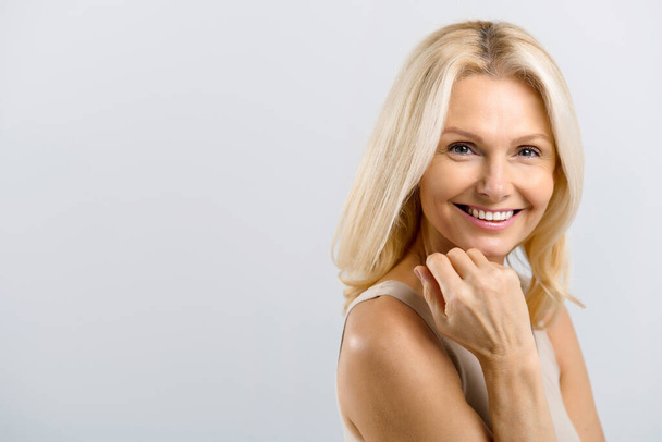 Middle-aged attractive blonde woman gently touching face and laughing - Fotografie, Obrázek