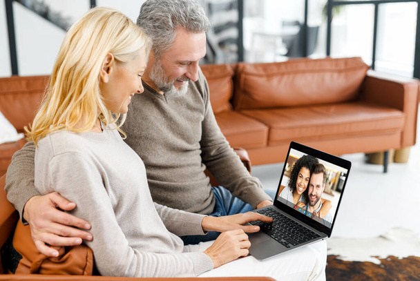 Middle-aged couple using laptop for video connection with grown children - Foto, imagen
