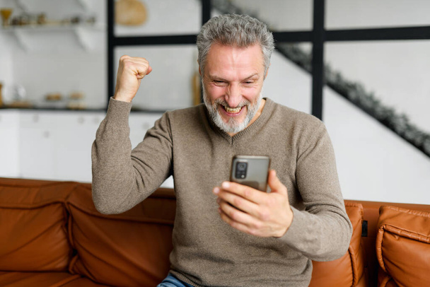 Senior grey-haired man is using smartphone for watching sports soccer match - Foto, imagen