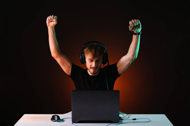 Игрок-победитель с наушниками, играющий в видеоигры на своем персональном компьютере - Фото, изображение