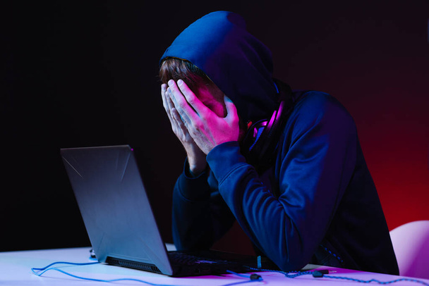 Професійний хакер з ноутбуком, що сидить за столом на темному фоні
 - Фото, зображення