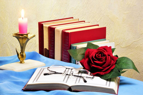 この本は、ヴィンテージキャンドル、読書用ガラス、創造的な休日のためのバラの花の装飾を背景に開いています。. - 写真・画像