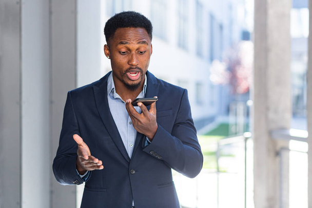 African American male businessman angry talking on mobile phone outside. Business man having phone call outdoors. Nervous mad professional conversation on smartphone. Irritated speak at urban street - Photo, image