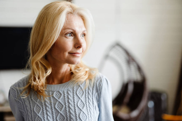 Smiling mid aged white blonde woman standing in modern room - Foto, Imagem