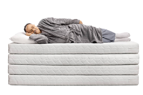 Mature man in a bathrobe sleeping on a pile of mattresses isolated on white background - Fotó, kép