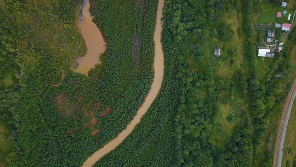 Ένα τεράστιο βρώμικο ποτάμι στο δάσος. Η θέα από το τηλεκατευθυνόμενο. Κλιπ. Μια τεράστια καμπυλότητα βρώμικο ποτάμι με προϊόντα πετρελαίου που ρέει δίπλα σε ένα τεράστιο πράσινο δάσος και πολλά μικρά σπίτια για τους ανθρώπους είναι - Φωτογραφία, εικόνα