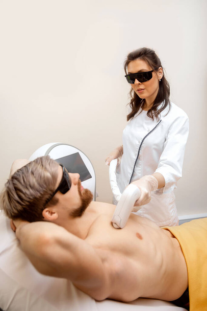 Woman worker beauty salon giving man torso hair removal laser epilation studio - Фото, изображение