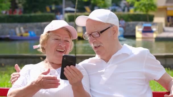 Šťastný starší pár s smartphone přičemž selfie a objímání v parku. - Záběry, video