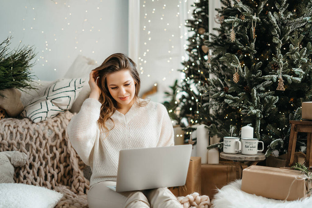 Sıcak kış kıyafetleri içinde, bilgisayar tabletlerine bakarak, Noel dileklerini okuyarak veya sosyal ağda yeni yıl gecesiyle arkadaşlarınızı tebrik ederek gülümseyen Kafkasyalı genç kadın.. - Fotoğraf, Görsel