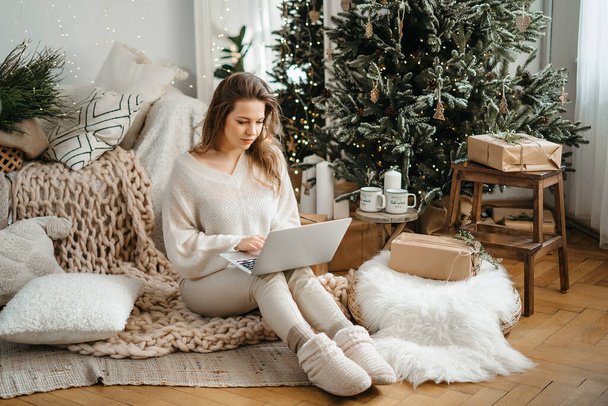Tête tourné souriant jeune femme caucasienne en vêtements chauds d'hiver regardant écran de tablette d'ordinateur, lire les vœux de Noël ou féliciter des amis avec la nuit du Nouvel An en ligne dans le réseau social. - Photo, image