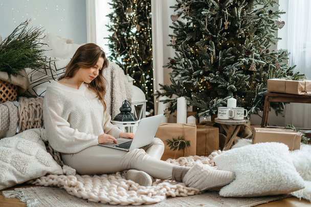 Fejlövés mosolygós fiatal kaukázusi nő meleg téli ruhák nézi számítógép tabletta ritkaság, olvasás karácsonyi kívánságok vagy gratuláló barátok szilveszter este online a közösségi hálón. - Fotó, kép