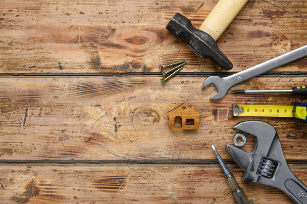 Arbeitswerkzeug und eine kleine Hausfigur auf einem alten Holzboden. Draufsicht, Leerraum links, selektiver Fokus auf das Haus. - Foto, Bild