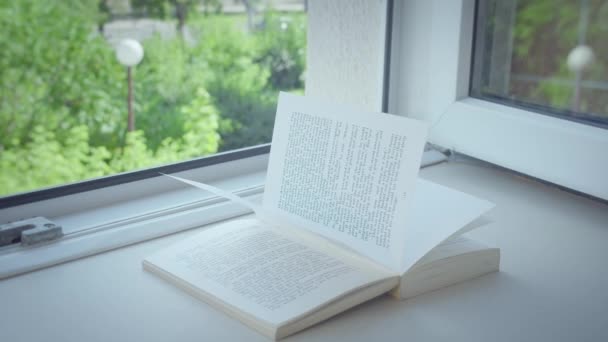 Otevřené okno na parapetu leží otevřená kniha, na stránkách svítí sluneční paprsek - Záběry, video