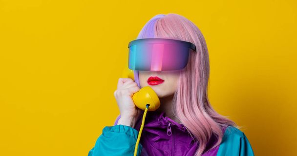 Tyyli nainen VR lasit ja 90s urheilu puku soittaa puhelimen keltaisella taustalla - Valokuva, kuva