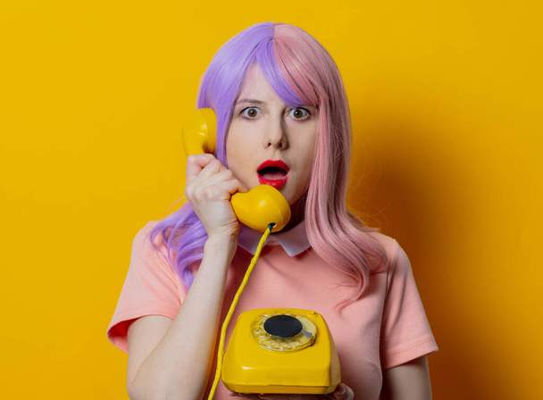 Girl with purple hair and pink dress hold dial phone on yellow background - Photo, image