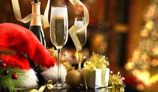 Christmas holidays celebration concept with bottle of sparkling white wine and glasses and christmas hat with gift and shiny ribbon decoration in living room. Front view. - Foto, imagen
