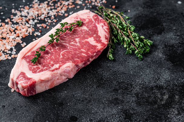 Rohe New-York-Streifen-Steak auf einem Metzgertisch mit Salz und Thymian. Schwarzer Hintergrund. Ansicht von oben. Kopierraum - Foto, Bild