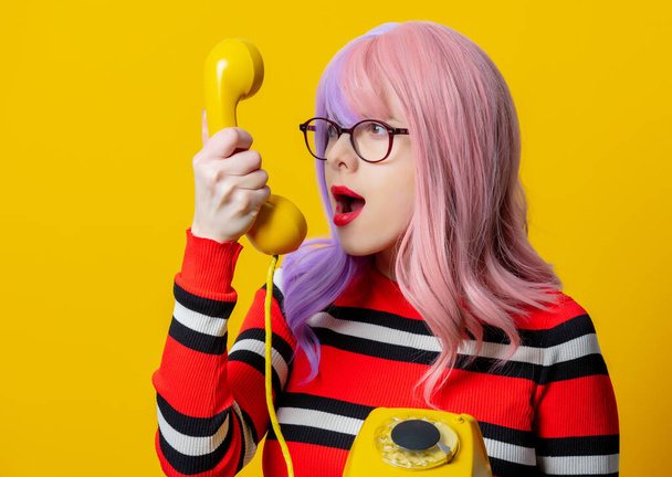 Meisje met paars haar en rode trui houden dial telefoon op gele achtergrond - Foto, afbeelding