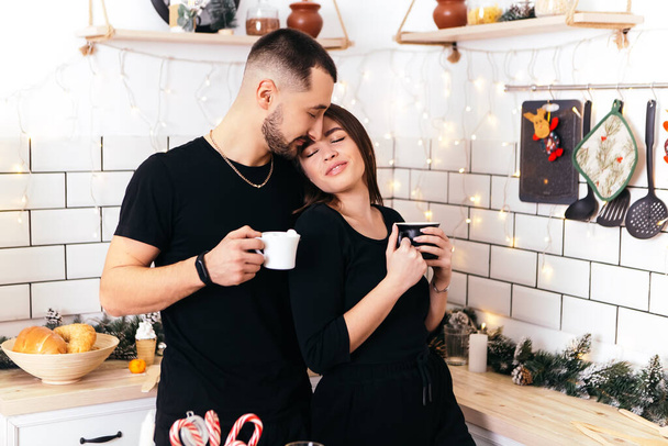 Lovely romantic couple standing kitchen drink hot beverage tea coffee home interior atmosphere New Year Christmas decorations mood holiday party celebrating concept winter evening copy space - Photo, Image