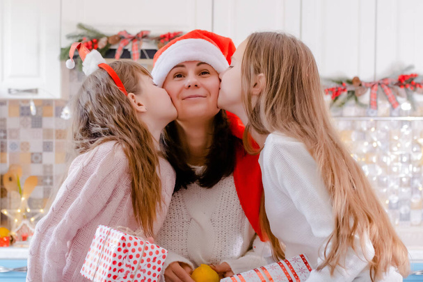 daughters kissing Happy mother in christmas decorated kitchen - Photo, Image