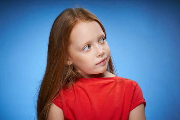 cute red-haired girl in red t-shirt emotions blue background - Foto, imagen