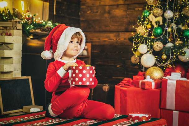 Child dressed in winter clothing think about Santa near Christmas tree. Merry Christmas for kids. - Foto, Imagem