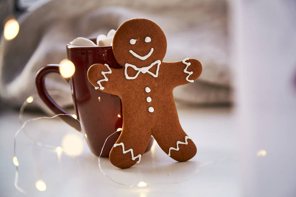 Symbol Vánoc - domácí perníková sušenka a rozmazaný bokeh dekor. Slavnostní vánoční ozdoby s teplým nápojem a marshmallows. Estetická vánoční atmosféra, domácí útulnost, koncept tepla - Fotografie, Obrázek