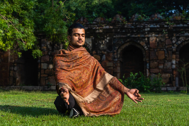 Yoga yapan genç kaslı bir adam ve güneşli bir günde çimenler üzerinde derin meditasyon yapan. - Fotoğraf, Görsel
