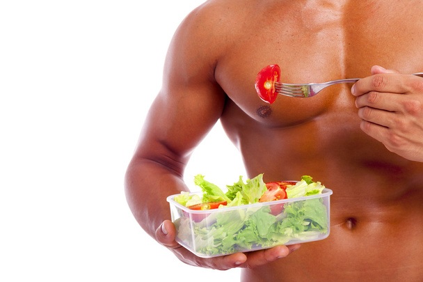 Close-up of a muscular man holding a bowl of fresh salad on a wh - Foto, Imagem