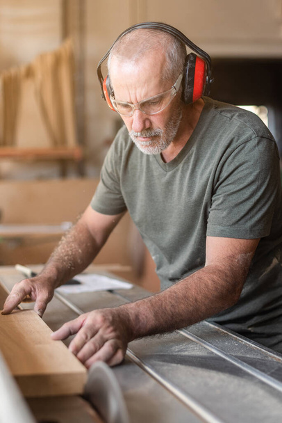 Muž s bezpečnostními brýlemi řezání dřeva na posuvném stole pilu - Fotografie, Obrázek
