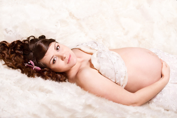 Pregnant woman lying on fur looking at camera. - Photo, Image