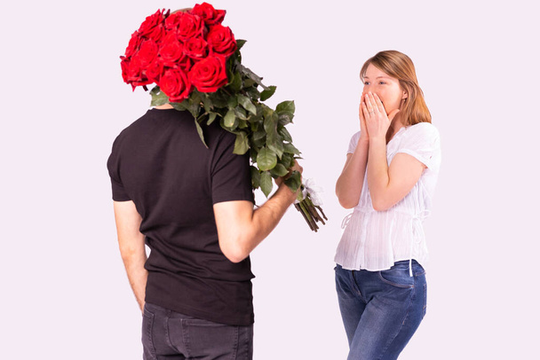 Courier man in black uniform delivered wonderful bouquet of red roses to a amazed blonde woman, she can not believe it and covers her face with her palms. - Photo, image