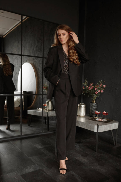 Graceful adult woman with stylish waved hairstyle wearing trendy black suit poses in the luxurious interior - Foto, Imagem