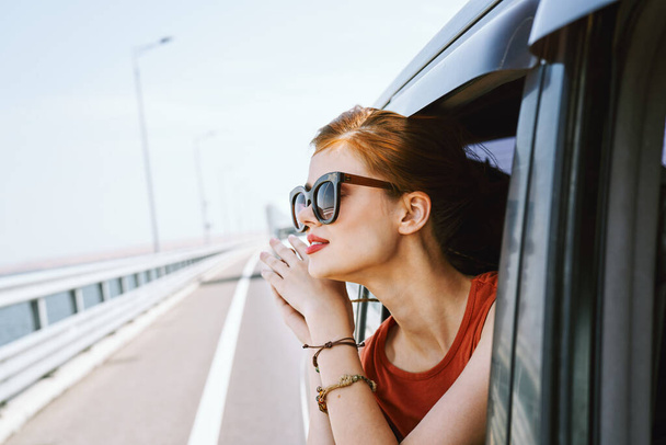žena dívá z okna auta nosí sluneční brýle cestovní životní styl - Fotografie, Obrázek