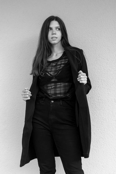 Portret van een jonge stijlvolle vrouw in zwarte kleding. Op een muurachtergrond. Zwart-wit foto. - Foto, afbeelding