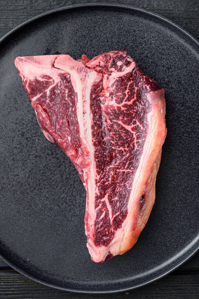 T-bone or Porterhouse for grill or BBQ set, on plate, on black wooden table background, top view flat lay - Photo, Image