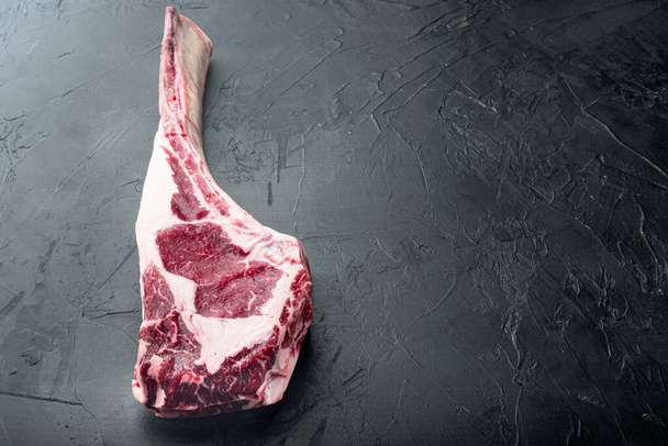 Roh Tomahawk Beef Steak mit Zutaten zum Grillen mit einem Gewürzreiben-Set, auf schwarzem Steinhintergrund, mit Kopierplatz für Text - Foto, Bild