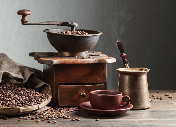 Taza de café negro, molinillo de café y frijoles asados en mesa de madera
 - Foto, Imagen