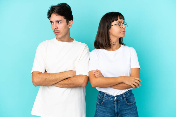 Mladá smíšená rasa pár izolované na modrém pozadí s matoucí výraz obličeje, zatímco kousne ret - Fotografie, Obrázek