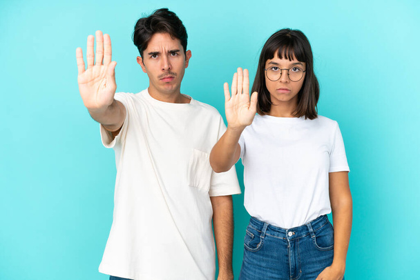Young mixed race couple isolated on blue background making stop gesture denying a situation that thinks wrong - Valokuva, kuva