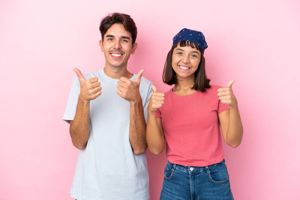 Young couple isolated on pink background giving a thumbs up gesture with both hands and smiling - Photo, Image