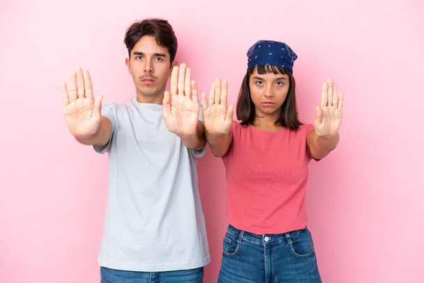 Giovane coppia isolata su sfondo rosa facendo gesto di stop per deluso con un parere - Foto, immagini