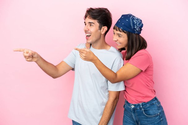 Fiatal pár elszigetelt rózsaszín háttér bemutatja egy ötlet, miközben nézett mosolyogva felé - Fotó, kép