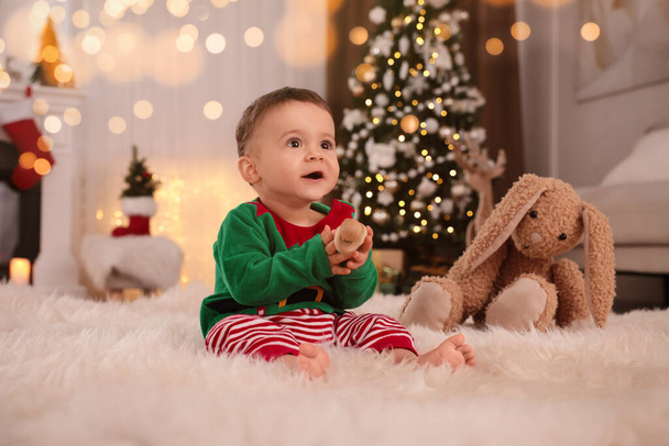 Baby wearing cute elf costume on floor in room decorated for Christmas - Fotoğraf, Görsel